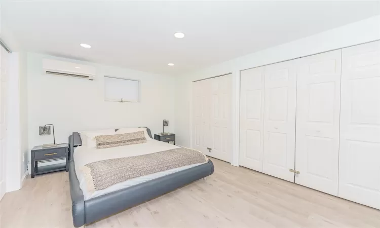 Bedroom with light wood-type flooring, two closets, and a wall unit AC