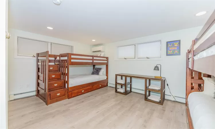 Bedroom with baseboard heating, a wall mounted AC, and light hardwood / wood-style floors