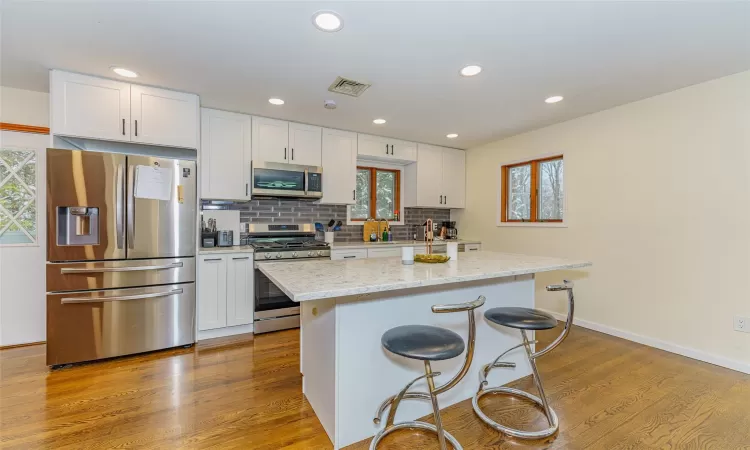 Kitchen with light hardwood / wood-style floors, a center island, white cabinetry, and appliances with stainless steel finishes