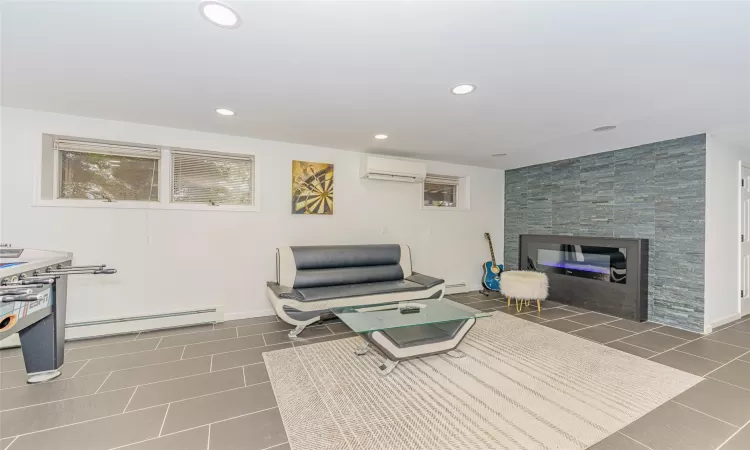 Living room with a stone fireplace, dark tile patterned flooring, a baseboard radiator, and a wall mounted air conditioner