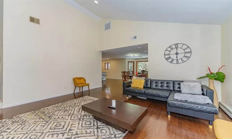 Living room with wood-type flooring, baseboard heating, and high vaulted ceiling