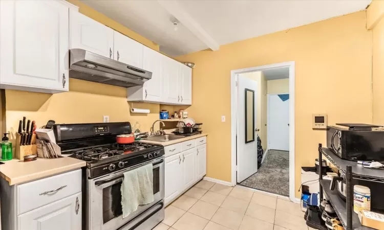 Kitchen featuring stainless steel gas stove, white cabinets, light tile patterned floors, and sink