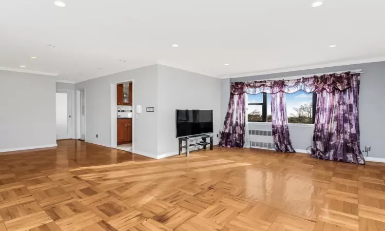 Unfurnished living room featuring crown molding, radiator, and light parquet flooring