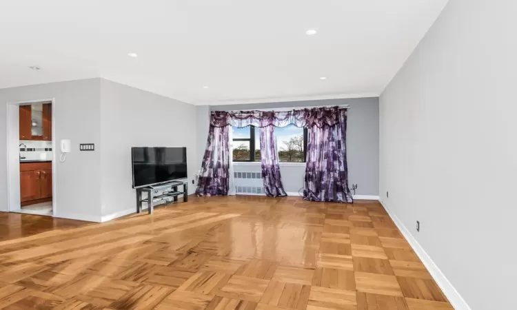 Unfurnished living room featuring radiator and light parquet floors