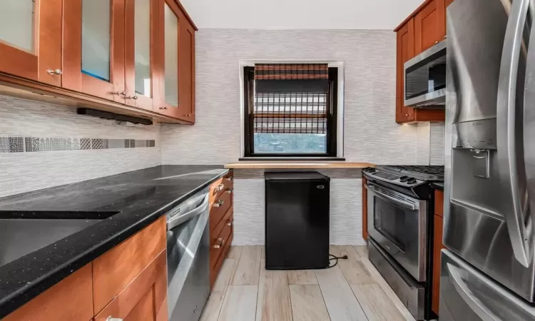 Kitchen featuring appliances with stainless steel finishes, light wood-type flooring, and dark stone counters