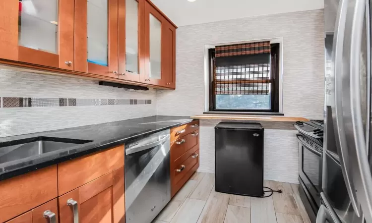 Kitchen with appliances with stainless steel finishes, tasteful backsplash, dark stone counters, and sink