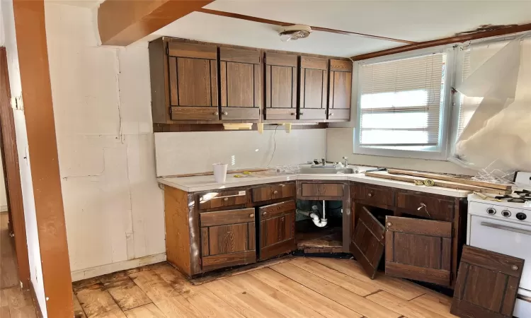 Kitchen featuring dark brown cabinets, light hardwood / wood-style floors, white range oven, and sink