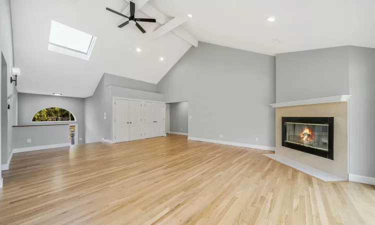 Unfurnished living room with ceiling fan, beam ceiling, high vaulted ceiling, light hardwood / wood-style flooring, and a fireplace