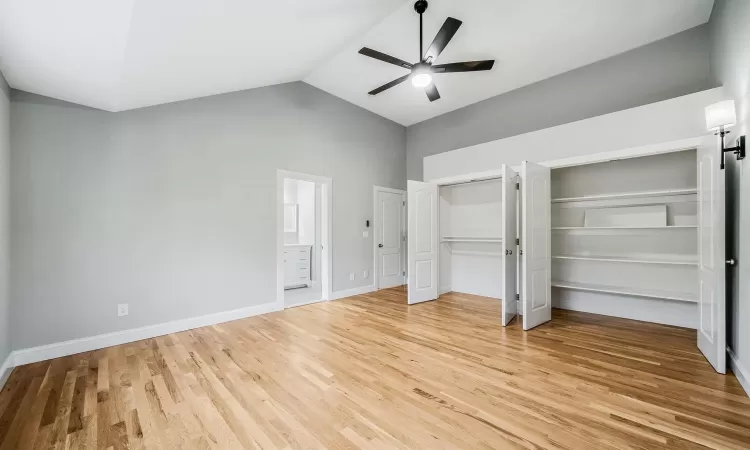 Unfurnished bedroom featuring connected bathroom, ceiling fan, light hardwood / wood-style flooring, high vaulted ceiling, and two closets