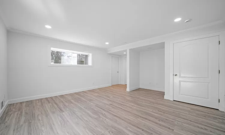 Basement with light hardwood / wood-style floors and crown molding