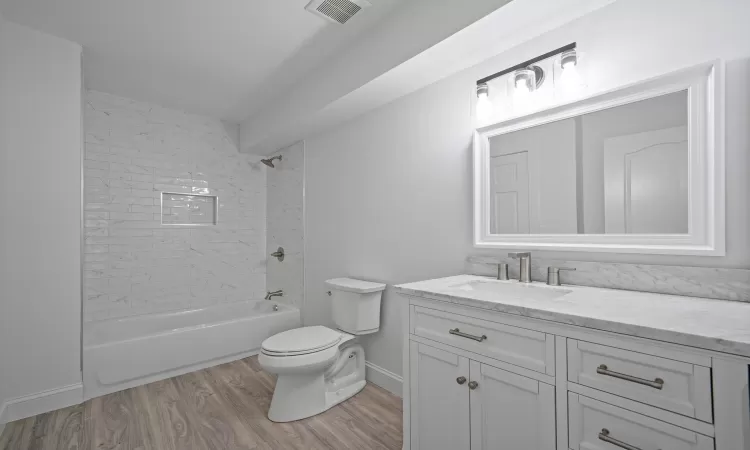 Full bathroom featuring vanity, tiled shower / bath combo, hardwood / wood-style flooring, and toilet