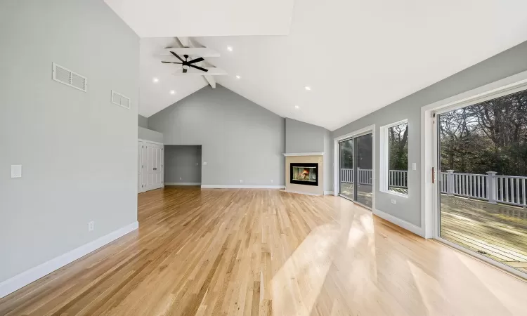 Unfurnished living room with ceiling fan, beam ceiling, light wood-type flooring, and high vaulted ceiling