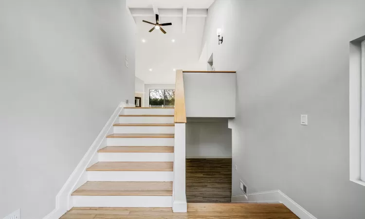 Stairway with hardwood / wood-style flooring, ceiling fan, beam ceiling, and a high ceiling