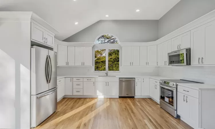 Kitchen with decorative backsplash, white cabinets, light wood-type flooring, and appliances with stainless steel finishes