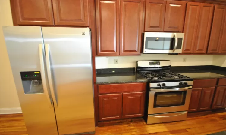 Kitchen with wood-type flooring, stainless steel appliances, and dark stone counters