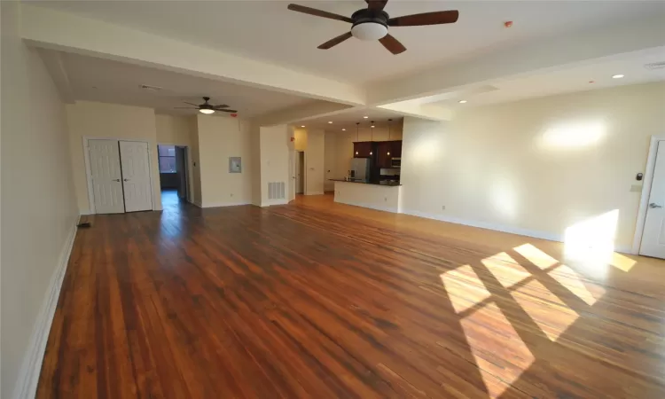 Unfurnished living room featuring ceiling fan, beamed ceiling, and dark wood-type flooring