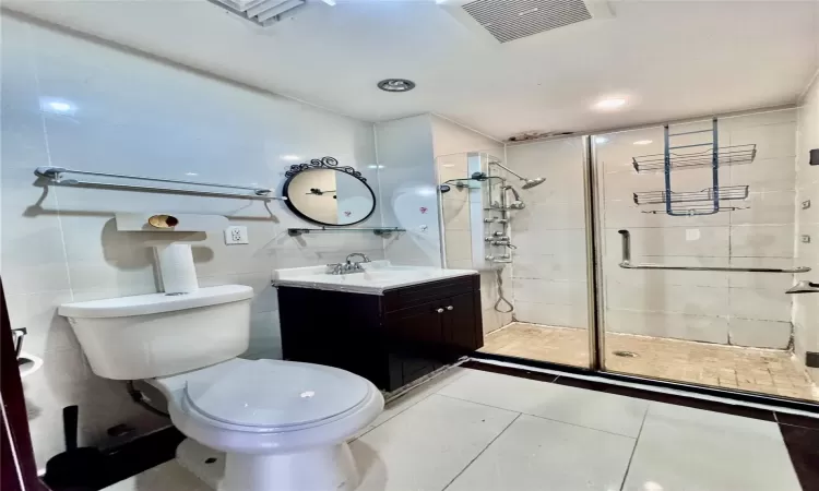 Bathroom with vanity, tile patterned flooring, toilet, tile walls, and an enclosed shower