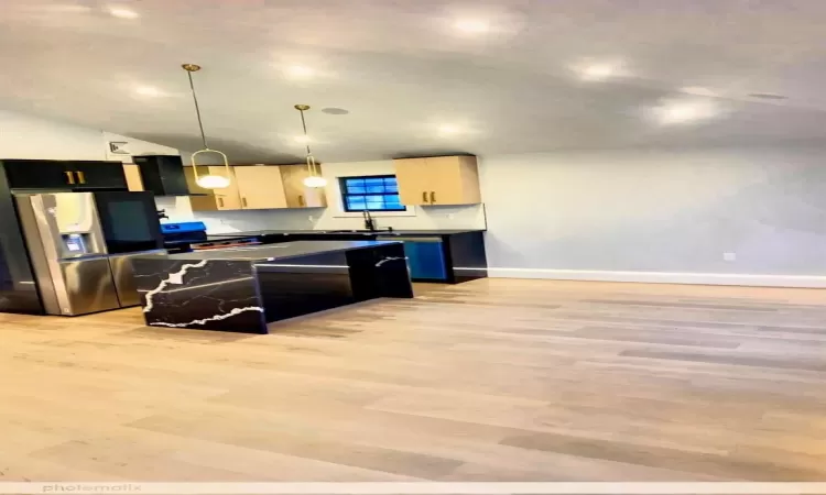 Kitchen with stainless steel fridge with ice dispenser, light wood-type flooring, hanging light fixtures, and light brown cabinets