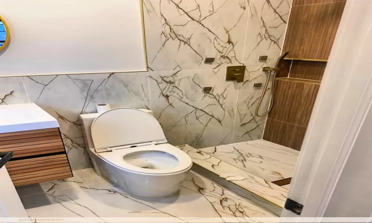 Bathroom with a shower, vanity, toilet, and tile walls