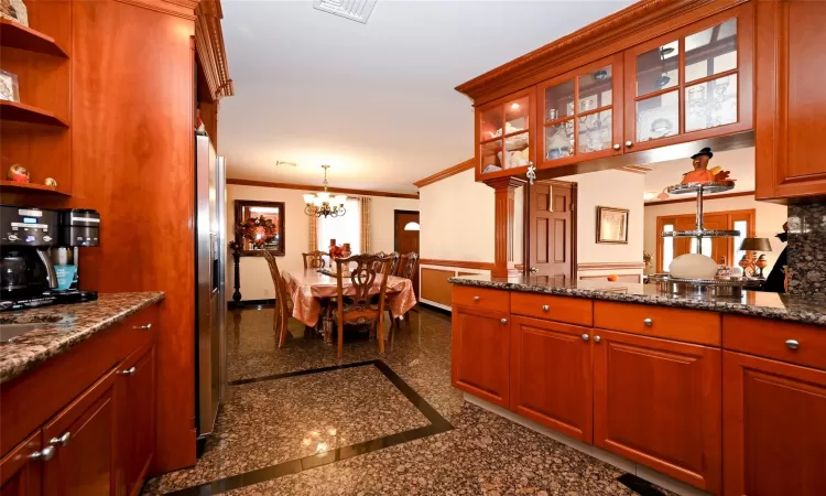 Kitchen featuring an inviting chandelier, stainless steel refrigerator with ice dispenser, crown molding, dark stone counters, and pendant lighting