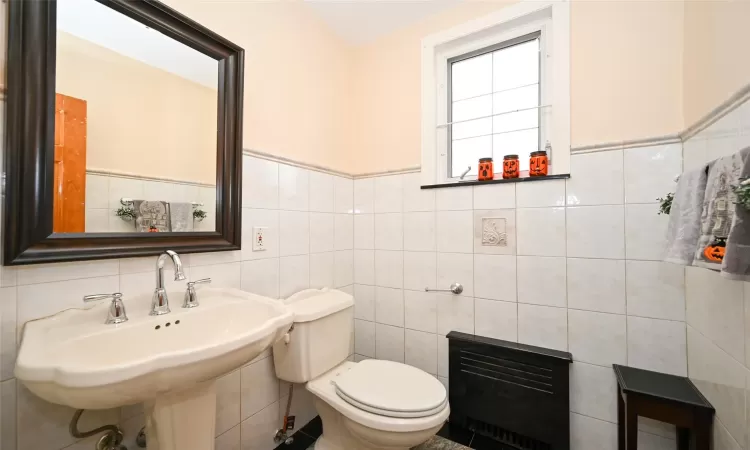 Bathroom featuring heating unit, toilet, tile walls, and sink