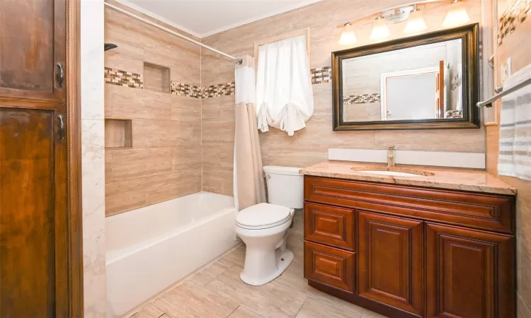 Full bathroom with vanity, shower / bath combination with curtain, crown molding, toilet, and tile walls