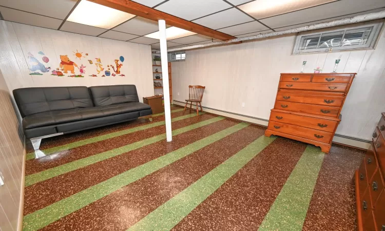 Basement with wooden walls, a drop ceiling, and a baseboard heating unit