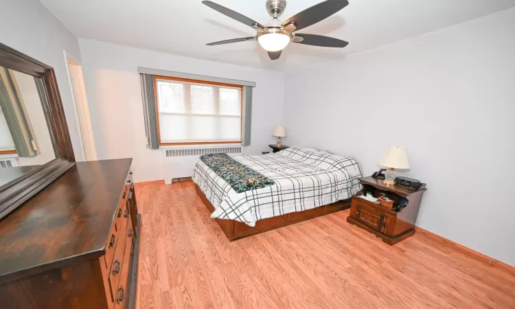 Bedroom featuring ceiling fan, radiator, and light hardwood / wood-style flooring