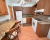 Kitchen featuring white appliances, dark stone counters, ventilation hood, sink, and light wood-type flooring