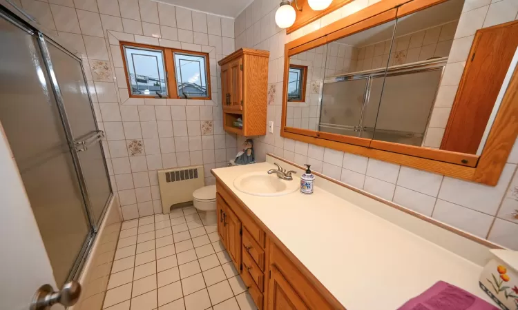 Bathroom featuring tile patterned floors, radiator heating unit, vanity, and tile walls