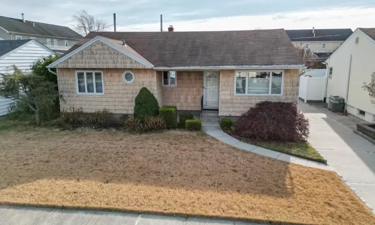 Ranch-style home featuring central air condition unit and a front lawn