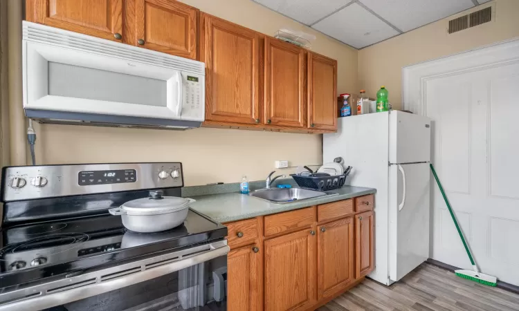 Kitchen with sink, a drop ceiling, white appliances, and light hardwood / wood-style floors