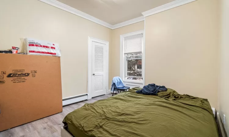 Bedroom with light hardwood / wood-style flooring, baseboard heating, and crown molding