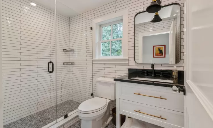 Bathroom with vanity, toilet, a shower with shower door, and tile walls