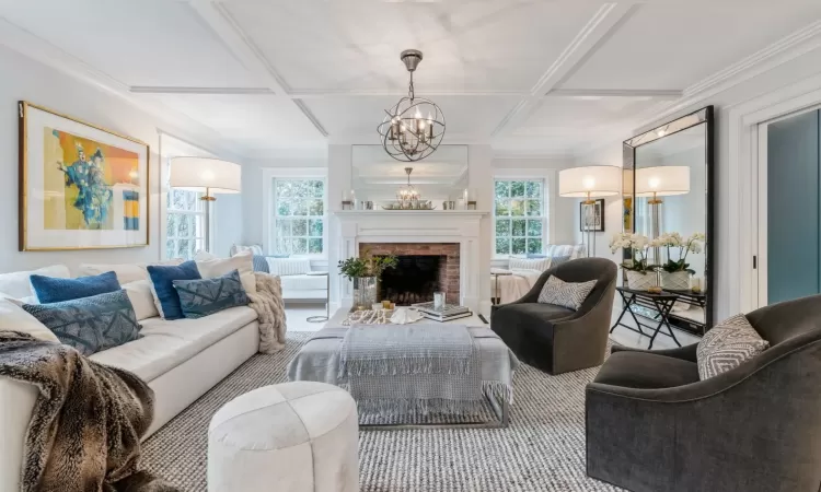 Living room with a fireplace, carpet floors, coffered ceiling, and a notable chandelier