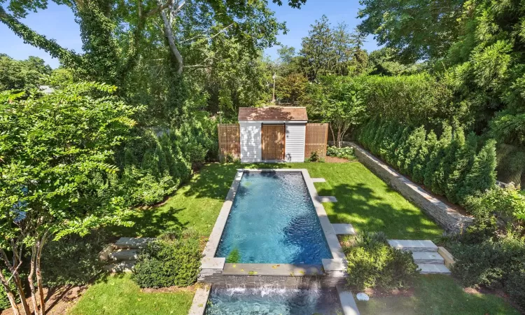 View of pool featuring a lawn, pool water feature, and a storage unit