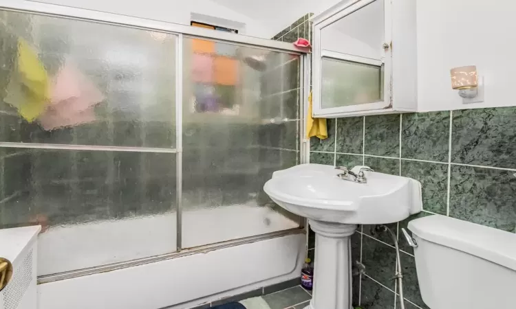 Bathroom featuring tile patterned flooring, combined bath / shower with glass door, toilet, and tile walls