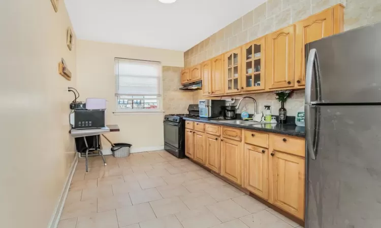 Kitchen with tasteful backsplash, stainless steel fridge, black gas stove, and sink