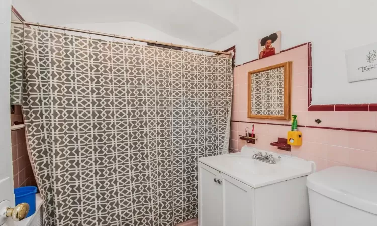 Bathroom featuring a shower with curtain, vanity, toilet, and tile walls