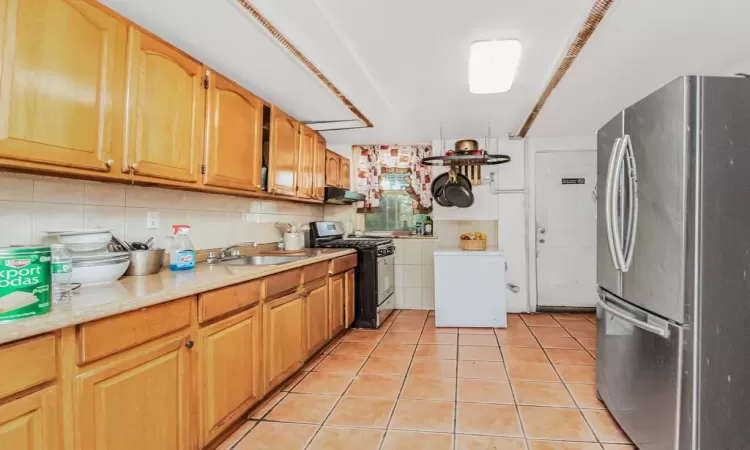 Kitchen with stainless steel refrigerator, sink, black range with gas stovetop, ventilation hood, and light tile patterned floors