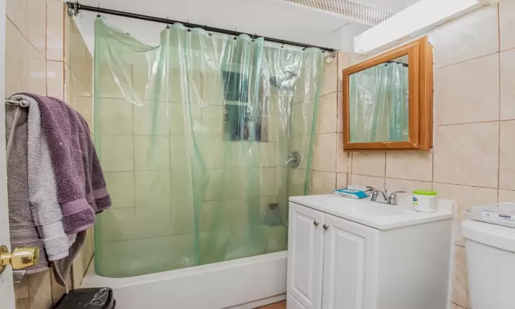 Full bathroom with vanity, toilet, tile walls, tasteful backsplash, and shower / tub combo