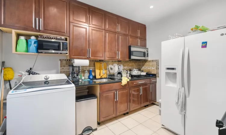 Kitchen featuring sink, white fridge with ice dispenser, backsplash, washer / dryer, and light tile patterned floors