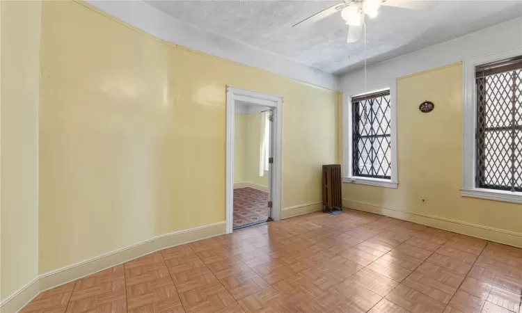 Empty room featuring radiator heating unit, light parquet floors, a healthy amount of sunlight, and a textured ceiling