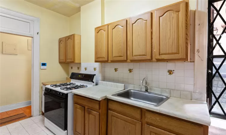 Kitchen featuring light tile patterned flooring, white gas range oven, tasteful backsplash, and sink