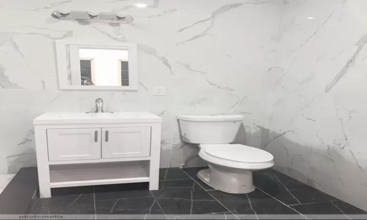 Bathroom with vanity, toilet, and tile walls