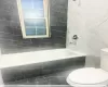 Bathroom with toilet, tiled shower / bath, and tile walls