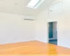 Unfurnished room featuring high vaulted ceiling, a skylight, a wall unit AC, and light hardwood / wood-style flooring