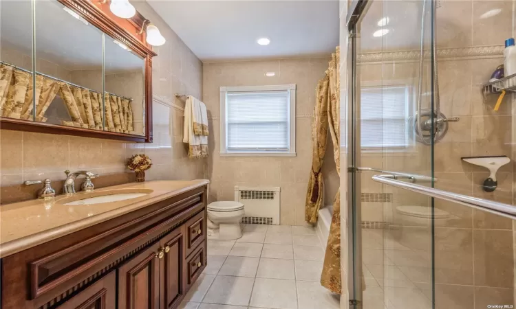 Bathroom with tile patterned floors, radiator, tile walls, and toilet