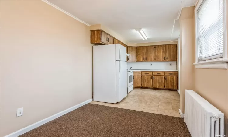 Kitchen with white appliances, light colored carpet, radiator, and crown molding