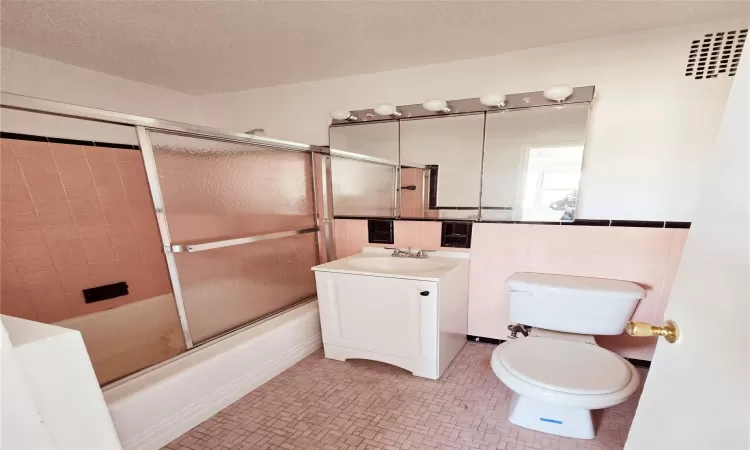 Full bathroom featuring tile patterned flooring, vanity, toilet, and bath / shower combo with glass door